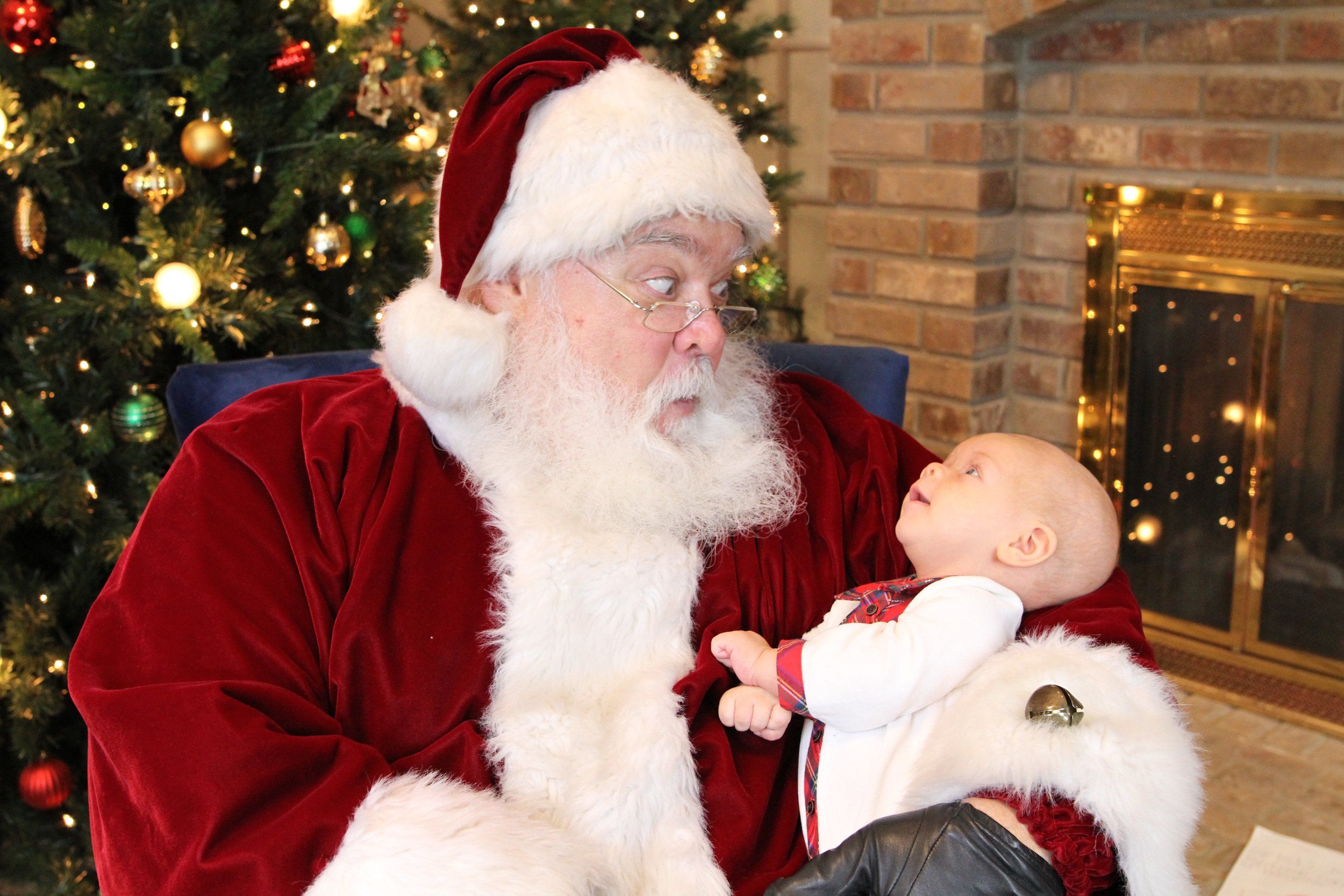 Santa holding an infant beside a Christmas tree